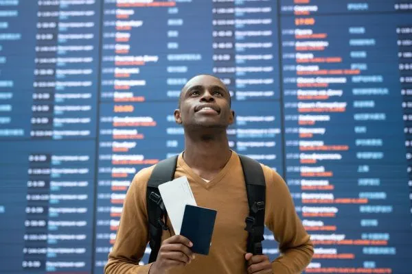 Mann am Flughafen steht vor einer Tafel mit Abflugzeiten